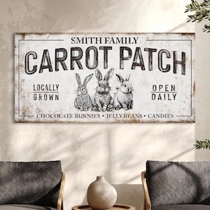 May include: A rectangular, distressed white sign with the text "SMITH FAMILY CARROT PATCH" in black. Below the text are three sketched bunnies. The sign also includes the phrases "LOCALLY GROWN" and "OPEN DAILY".