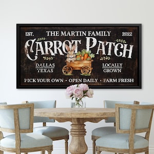 May include: A framed sign with the text "Carrot Patch" and a watercolor illustration of a bunny in a cart of carrots. The sign also includes the text "Dallas Texas" and "Locally Grown". The sign is displayed above a wooden table and chairs.