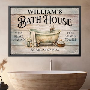 May include: A framed wooden sign with the text "WILLIAM'S BATH HOUSE" above an antique bathtub illustration. The sign includes the phrases "SOAK, RELAX, UNWIND" and "FREE SOAP & TOWELS". Established 2023 is also printed on the sign.