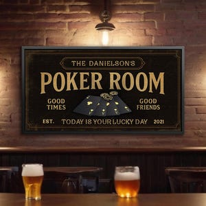 May include: A framed sign with the text "POKER ROOM" in gold lettering. The sign includes the text "The Danielson's", "Good Times", "Good Friends", and "Today is Your Lucky Day 2021". The sign also features playing cards and poker chips.