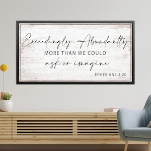 May include: A rectangular wall sign with a black frame and a white, distressed wood-look background. The text reads: Exceedingly, Abundantly MORE THAN WE COULD ask or imagine EPHESIANS 3:20 in a mix of black script and block lettering.