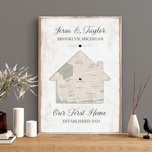 May include: A framed wooden sign with the text "Jessa & Taylor, Brooklyn, Michigan" above a house-shaped map. The words "Our First Home, Established 2023" are below the map. The sign is on a wooden surface.