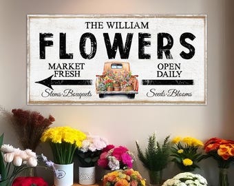May include: A rectangular wooden sign with the words "The William Flowers" in large black letters. Below the text is a vintage truck filled with flowers. The sign also includes the phrases "Market Fresh", "Open Daily", "Stems Bouquets", and "Seeds Blooms".