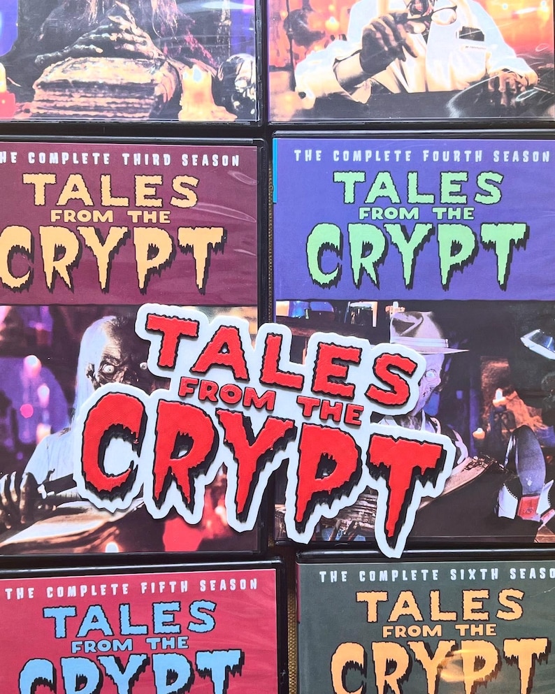May include: A selection of DVD cases for "Tales From The Crypt." The cases are in shades of red, purple, and green, with the show's logo clearly visible. A sticker bearing the show's logo is also present in the image.