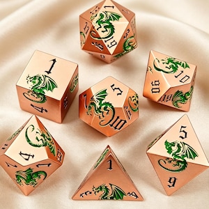 Könnte beinhalten: Ein Set aus sieben polyedrischen Würfeln in metallischem Roségold. Jeder Würfel ist mit detaillierten grünen Drachenillustrationen und schwarzen, in gotischer Schrift eingravierten Zahlen versehen. Das Set enthält W20, W12, W10, W8, W6, W4 und einen W100.