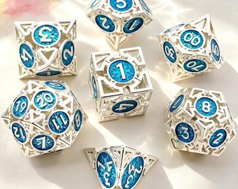 May include: A set of seven silver metal dice with blue enamel details. Each die features a unique geometric design with numbers in white. The dice are designed for role-playing games and are displayed on a light background.