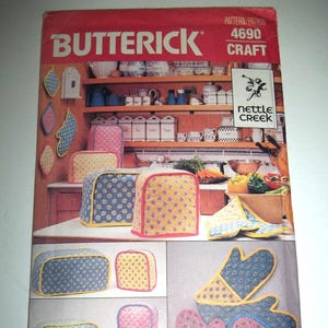 May include: A vintage sewing pattern from Butterick, pattern number 4690, for kitchen accessories. The pattern is for a set of oven mitts, toaster covers, and bread machine covers. The pattern is from the Nettle Creek line. The pattern features a floral print in blue, yellow, and pink.