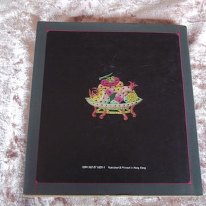 Op de afbeelding: De achterkant van een boek met een kleurrijke illustratie van een mand vol fruit met een haan erop. De tekst "ISBN 962 87 5029 4 Published & Printed in Hong Kong" staat onderaan de omslag gedrukt.