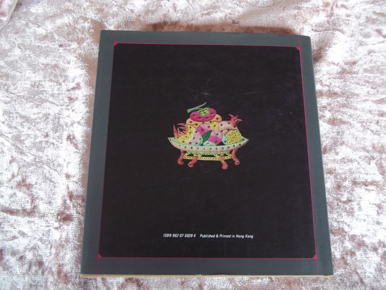 Op de afbeelding: De achterkant van een boek met een kleurrijke illustratie van een mand vol fruit met een haan erop. De tekst "ISBN 962 87 5029 4 Published & Printed in Hong Kong" staat onderaan de omslag gedrukt.