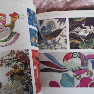 Op de afbeelding: Een boek met kleurrijke geborduurde afbeeldingen van vogels en bloemen. Het boek heeft paginanummers 143, 148, 149 en 150.