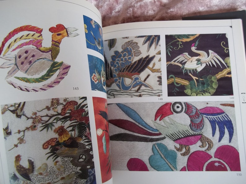 Op de afbeelding: Een boek met kleurrijke geborduurde afbeeldingen van vogels en bloemen. Het boek heeft paginanummers 143, 148, 149 en 150.