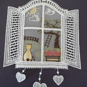 May include: A white lace window hanging with an embroidered scene. The window frame is open, revealing a sunny day with a cat, tree, and flowers. Three white lace hearts dangle below the window.