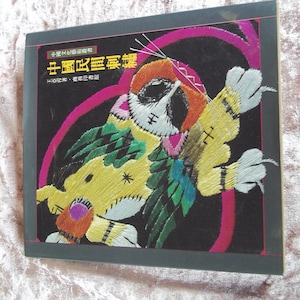 Op de afbeelding: Een boekomslag met een kleurrijk geborduurd beeld van een vogel met een roze, gele en groene ontwerp. De titel van het boek is "十字繡圖案集", wat vertaalt naar "Collectie van kruissteekpatronen".