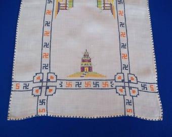 May include: A white linen tea towel with a stitched design of a pagoda and a border of swastikas.