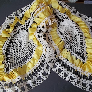 Puede incluir: Un mantel de crochet blanco con un ribete de cinta de satén amarillo. El mantel tiene un borde festoneado y un delicado patrón floral.