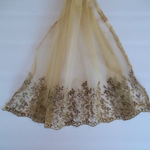 Puede incluir: Una tela beige transparente con un delicado ribete de encaje floral marrón. La tela es ligera y translúcida, con una textura suave y fluida.