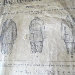 Op de afbeelding: Een oud papier met illustraties van jongenspakken, inclusief jassen en knickerbockers. De tekst luidt "Prijs, 25 Cent" en geeft maten per leeftijd en borstomvang in inches. Het papier is versleten en verouderd.