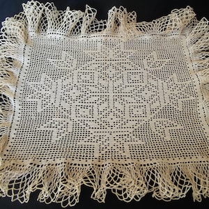 May include: A delicate, off-white crocheted doily with a lacy border. The doily features a repeating pattern of squares and circles.