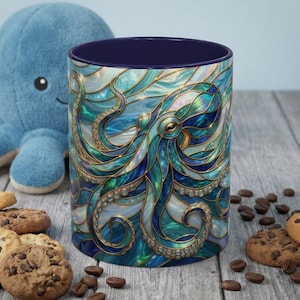 May include: A ceramic mug with a stained-glass octopus design in shades of blue, teal, and gold. The mug has a dark blue interior and is surrounded by cookies, coffee beans, and a blue plush octopus toy.