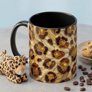 May include: A ceramic coffee mug with a black handle and interior, featuring a leopard print design in shades of brown and gold. A stuffed leopard toy and coffee beans are next to the mug.
