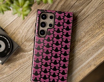 May include: A black phone case with a pink bow pattern. The case has a camera cutout on the back.