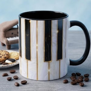 May include: A ceramic mug featuring a piano keyboard pattern with black and white marble-effect keys separated by thin gold lines. The mug has a solid black interior and a matching black handle, presenting a sleek design with a glossy finish.