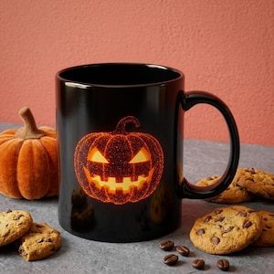 May include: A black ceramic mug featuring a glowing orange jack-o'-lantern graphic with a glittery texture. The mug is surrounded by several chocolate chip cookies and a small orange fabric pumpkin, set against a solid coral-colored background.