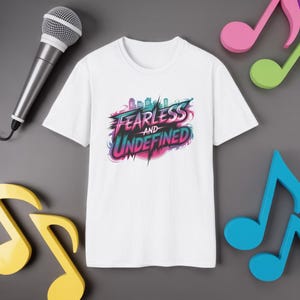 May include: White t-shirt with the words "FEARLESS AND UNDEFINED" in a colorful, stylized design. A silver microphone and colorful musical notes surround the shirt, suggesting a music or performance theme.