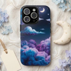 Pode incluir: Capa de smartphone com um design de céu noturno sonhador com nuvens roxas e azuis fofas, uma lua crescente e estrelas. A capa tem uma borda preta e um acabamento brilhante. Uma etiqueta em branco e uma lua de pelúcia estão no fundo.