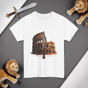 May include: White t-shirt featuring a graphic of the Colosseum with a sword in front. The words "STRENGTH & HONOR" are printed below the image. A toy lion and sword are also in the image.
