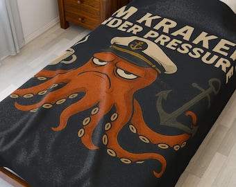 Op de afbeelding: Een zwart en oranje deken met een cartoon octopus die een kapiteinshoed draagt. De tekst "I'm Kraken Under Pressure" is op de deken gedrukt.