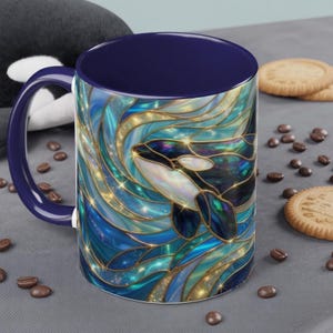 May include: A ceramic mug with a blue interior and handle. The exterior features a stained-glass style design of a killer whale in shades of blue, teal, and gold. Coffee beans and cookies are scattered around the mug.