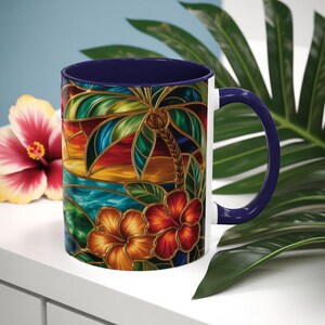 May include: White ceramic mug with a stained-glass design featuring a palm tree, hibiscus flowers, and a sunset scene. The mug has a dark blue interior and handle. A red and yellow hibiscus flower is in the background.
