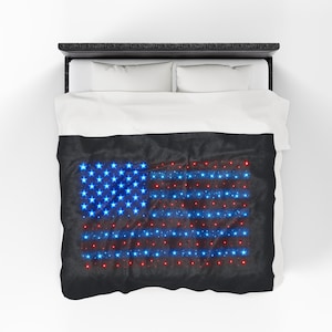 May include: A black bedspread with a glowing American flag design. The flag's stars are blue, and the stripes are red, with a sparkling effect. The bedspread is on a bed with white pillows and sheets.