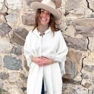 May include: A cream-coloured poncho with fringe trim and a matching hat. The poncho has a hood and is fastened with two wooden buttons. The text "Winter Pearl" is at the bottom right.