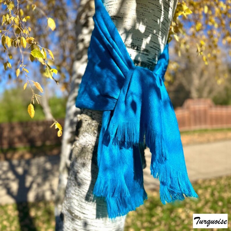 May include: A bright turquoise scarf with fringed edges is wrapped around a tree trunk. The scarf's colour is a vivid blue-green, and the fringe adds texture. The word "Turquoise" is in the bottom right corner.