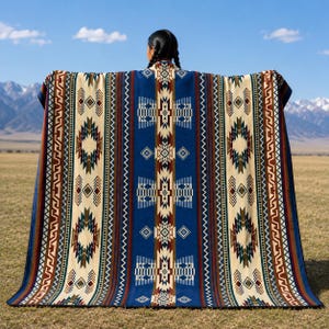 May include: A large rectangular blanket featuring a central vertical blue panel with geometric patterns, flanked by cream-coloured sections with repeating diamond and zigzag motifs in shades of brown, dark blue, and red, with a dark blue border.
