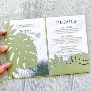 May include: Green wedding invitation with a cut-out tropical leaf design. The invitation text reads "You are joyfully invited to celebrate the wedding of Kimberly Uftring and her [unclear] on August 27, 2022 at [unclear] Country Club. Details include reception information, directions, and accommodations.  The invitation is folded in half.
