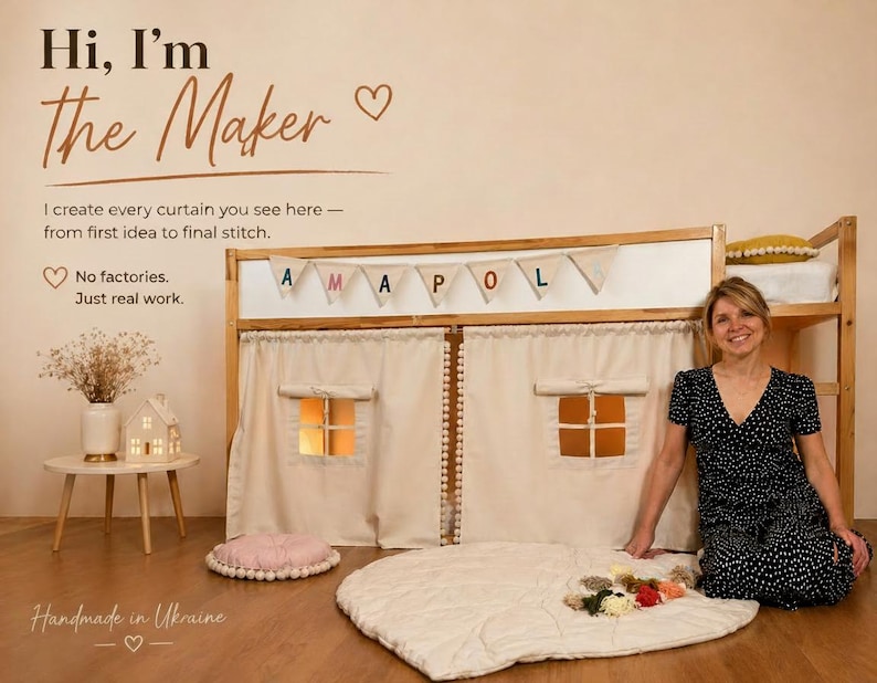 May include: A beige fabric playhouse curtain set attached to a wooden bed frame, featuring two windows with roll-up shades, a pom-pom trim, and a bunting banner spelling AMAPOLA. The curtain is made of solid light-colored fabric with stitched details.