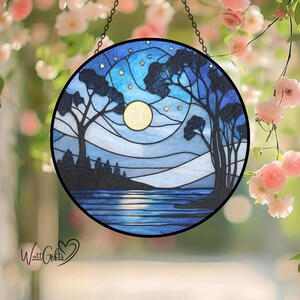 May include: Round stained glass panel depicting a nighttime landscape with a full moon, stars, and silhouetted trees. The panel features shades of blue and white, with a black border and chain for hanging. The image is set against a blurred floral background.