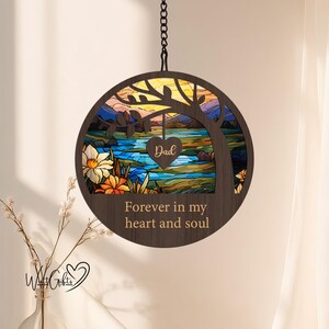 May include: A wooden hanging ornament with a stained glass design of a tree, lake, and sunset. The ornament has the text "Forever in my heart and soul" and a heart with the word "Dad" on it.