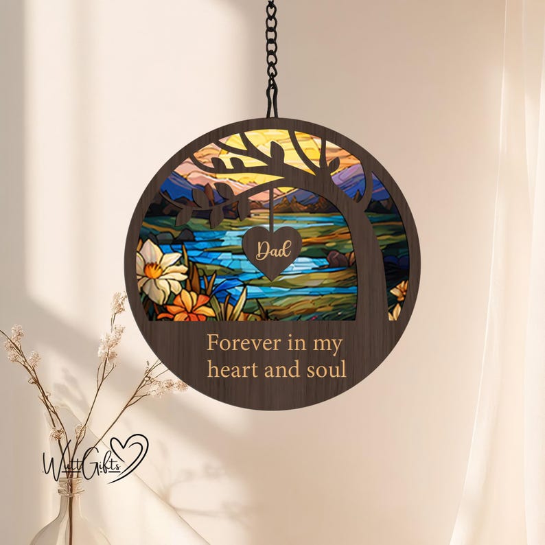 May include: A wooden hanging ornament with a stained glass design of a tree, lake, and sunset. The ornament has the text "Forever in my heart and soul" and a heart with the word "Dad" on it.