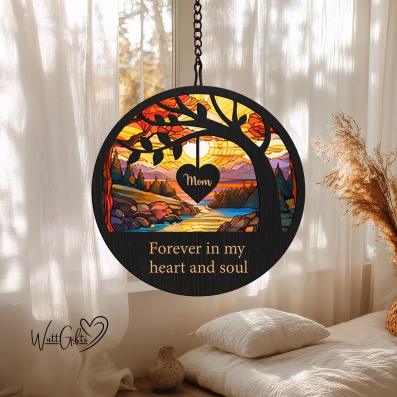 May include: A round wooden hanging ornament with a stained glass design of a tree and a sunset. The ornament has the text "Forever in my heart and soul" and a small heart with the word "Mom" on it.