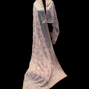 Op de afbeelding: Een lichtroze sjaal met ingewikkelde bloemenborduurwerk en een delicate rand. De sjaal is over een zwarte mannequin gedrapeerd, wat het vloeiende ontwerp en het gedetailleerde vakmanschap benadrukt. De borduursels bevatten zilveren en gouden draden.