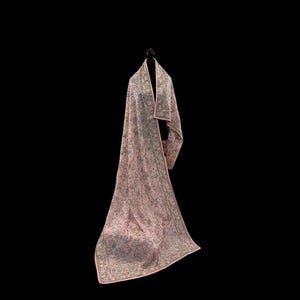 Op de afbeelding: Een lange, roze sjaal met een ingewikkeld bloemenpatroon en een contrasterende roze rand. De sjaal is over een zwarte mannequin gedrapeerd, wat de lengte en het ontwerp laat zien. De stof lijkt zacht en vloeiend.