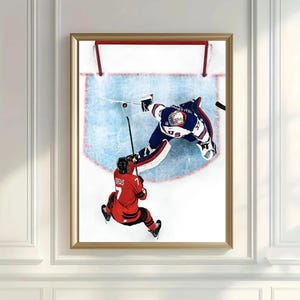 May include: A framed print of a hockey game in action. Two players are visible, one in red and one in blue, with the puck near the goal. The image is set against a white background.