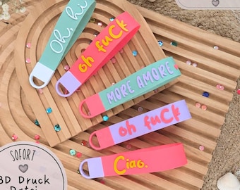 May include: Five silicone wristlet keychains in various colors including mint, pink, lavender, and coral. Each features raised text: Oh, hi, oh fuCk, MORE AMORE, oh fuCk, and Ciao. The keychains have a loop at one end for attachment.