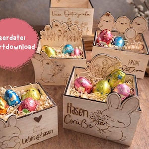 Könnte beinhalten: Verschiedene Holzboxen zum Thema Ostern mit Laserschnitt-Designs. Jede Box enthält bunte Ostereier, eingebettet in Stroh. Einige Boxen zeigen Hasen- und Blumenmotive sowie Texte wie "Liebe Ostergrüße" und "Frohe Ostern".