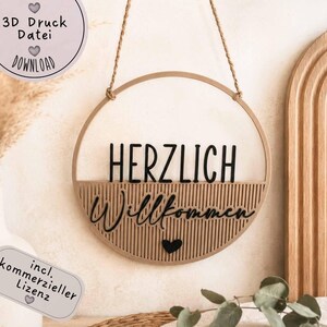Puede incluir: Un letrero redondo de madera con las palabras "HERZLICH Willkommen" en letras negras. El letrero está suspendido por una cuerda natural y presenta un símbolo de corazón. Texto adicional: "SOFORT 3D Druck Datei DOWNLOAD".