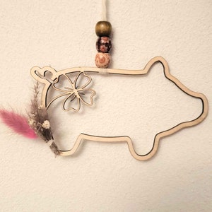 May include: A wooden cutout of a pig with a four-leaf clover design. The pig is hanging from a string with three wooden beads.